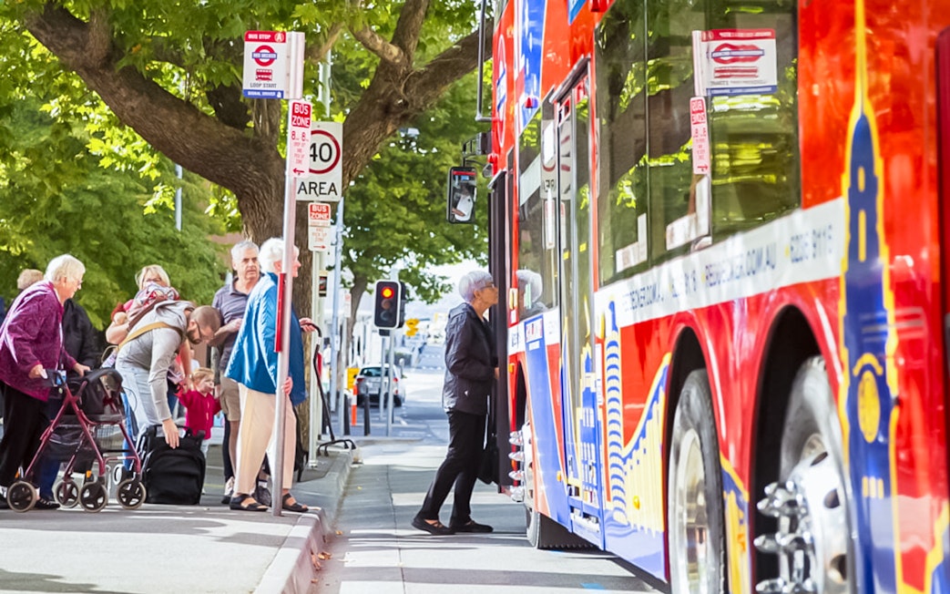 People boarding a red Hobart hop-on hop-off bus at a city stop.