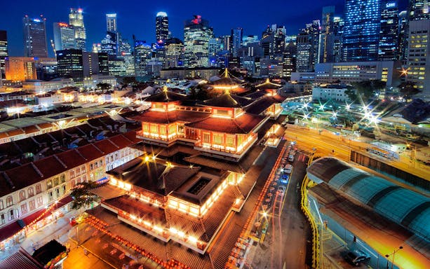 Buddha Tooth Relic Temple illuminated at night with Singapore skyline in the background.