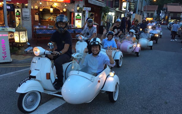 Group enjoying a vintage Vespa sidecar tour at night in Singapore street.