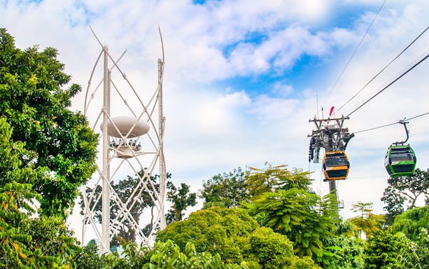 SkyHelix Sentosa ride and cable cars above lush greenery in Sentosa, Singapore.