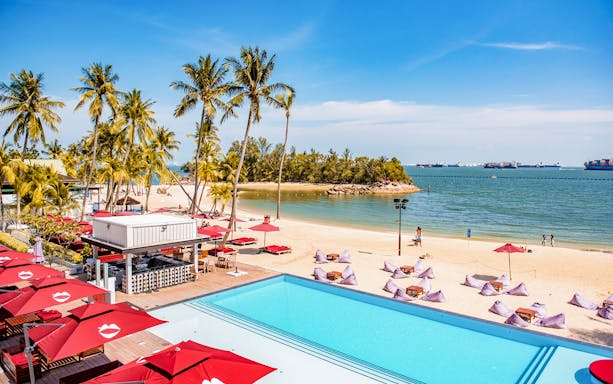 Sentosa beach view with palm trees, pool, and dining area, part of SkyHelix Sentosa tour.