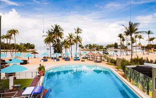 Sentosa beach view with pool, palm trees, and cabanas, part of SkyHelix Sentosa tour.