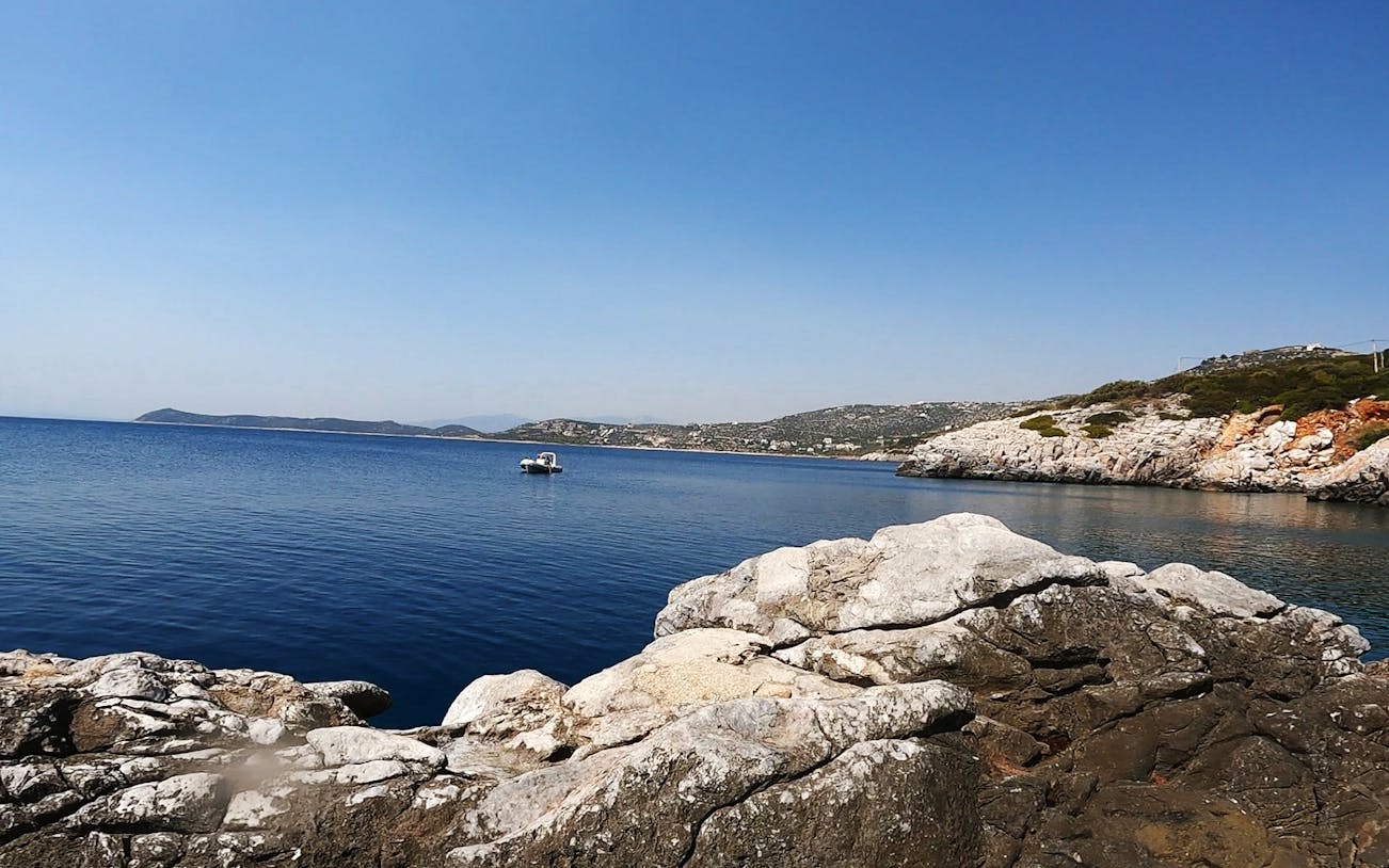 Boat near rocky coastline in Nea Makri, Athens, ideal for cliff diving trips.