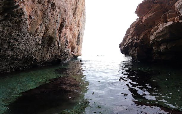 Cliffside view of a boat in a sea cave during a Nea Makri cliff diving trip, Athens.