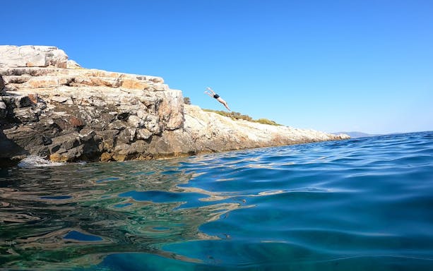 Cliff diver mid-air above rocky coastline in Nea Makri, Athens.
