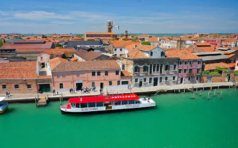Hop-on hop-off boat at Murano Island, Venice, with colorful buildings and canal.