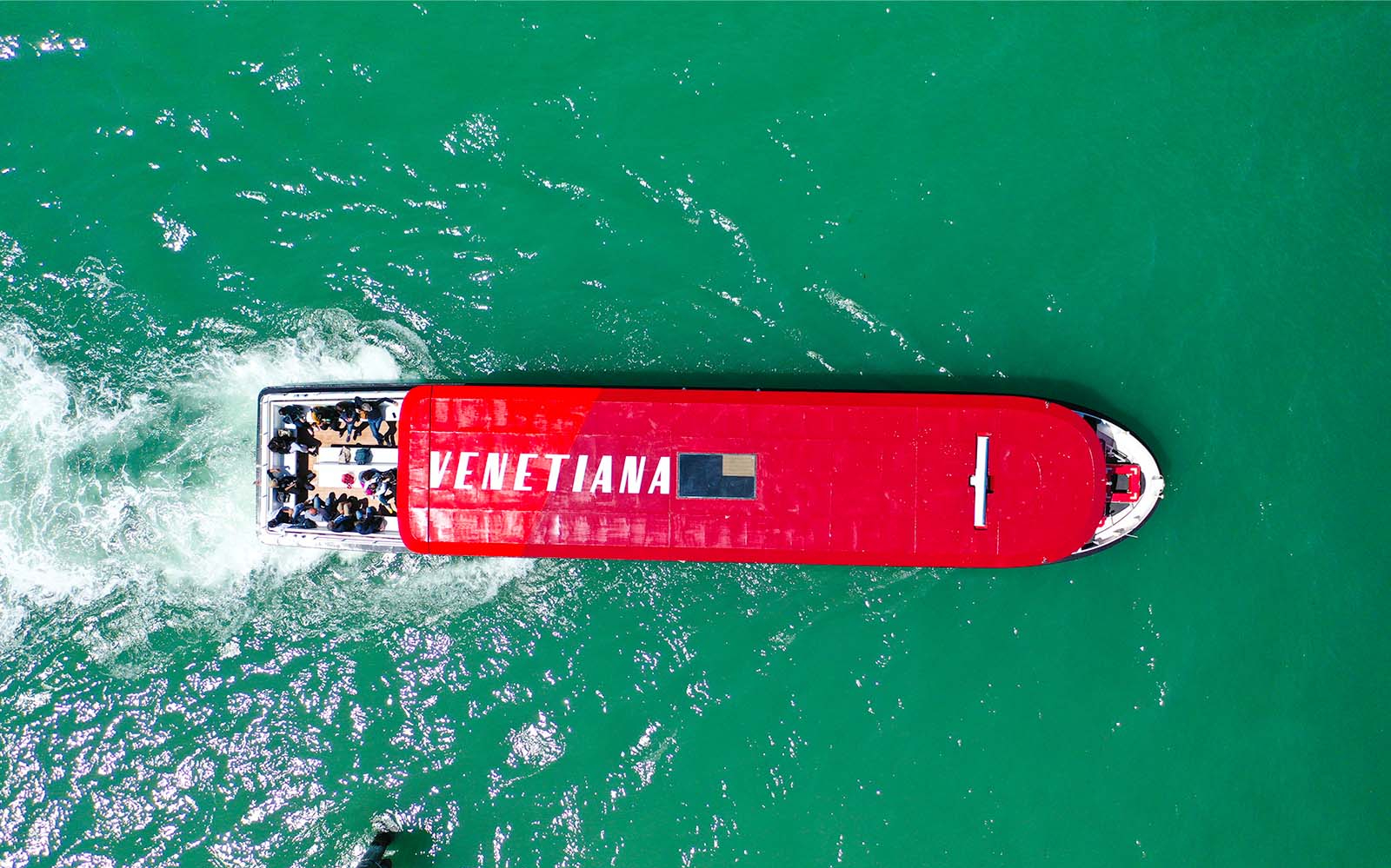 Hop-on hop-off boat with passengers on Venice's turquoise waters.