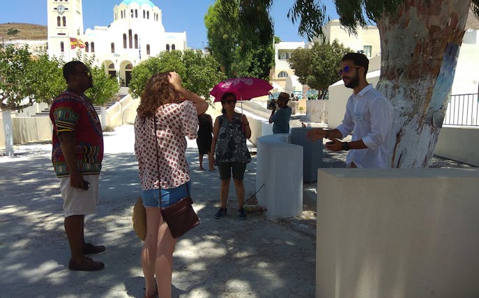 Tourists gather near a guide in front of a church during a Santorini sightseeing bus tour.