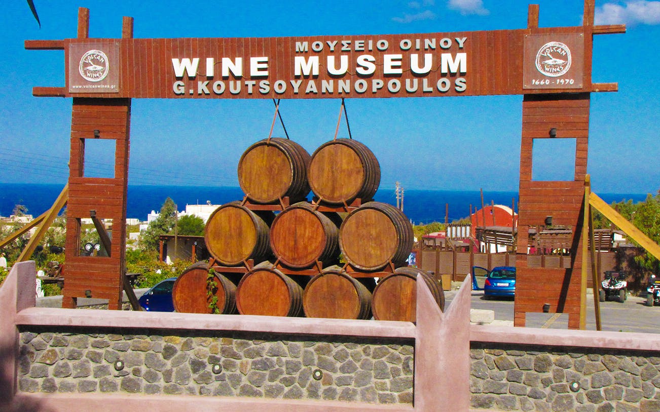 Santorini Wine Museum entrance with stacked barrels and sea view.