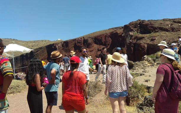 Tourists exploring the Red Beach cliffs on a Santorini sightseeing bus tour.