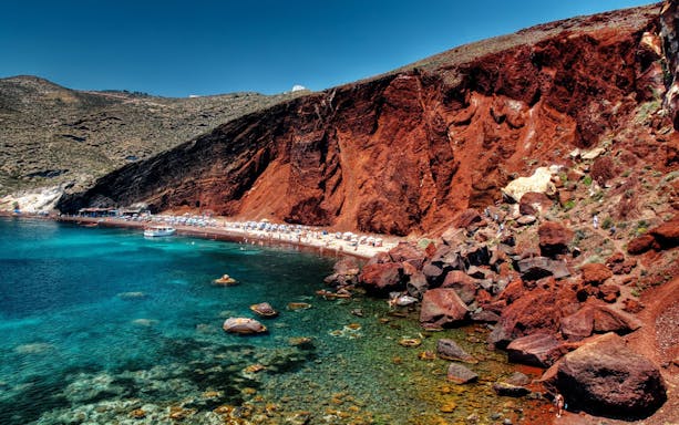 Red Beach cliffs and turquoise waters in Santorini, Greece, seen on a sightseeing bus tour.