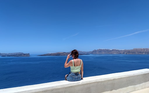 Woman sitting on a ledge overlooking the Aegean Sea in Santorini, Greece.