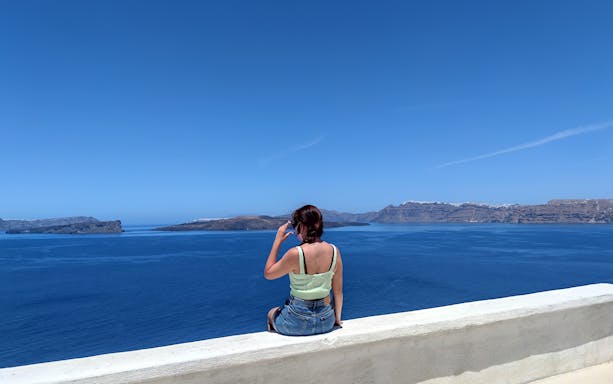 Woman sitting on a ledge overlooking the Aegean Sea in Santorini, Greece.