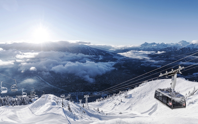 Cable car ascending snowy mountain with view of Innsbruck and Alps.