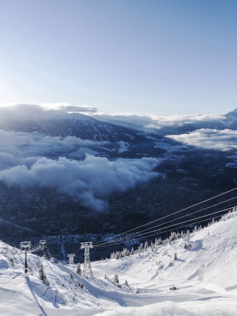 Cable car ascending snowy mountain with view of Innsbruck and Alps.