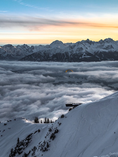 Paraglider over snowy Alps at sunset, Top of Innsbruck PLUS.