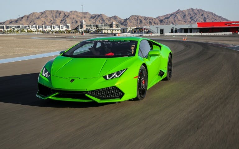 Lamborghini driving on a racetrack with mountains in the background.