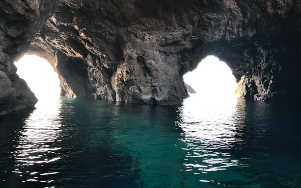 Sea cave entrance with sunlight, Delos and Rhenia islands cruise.
