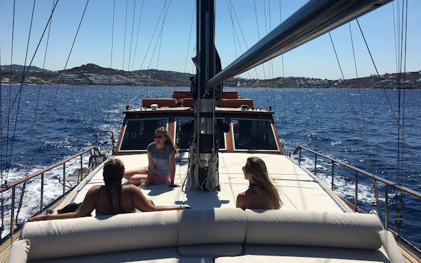 Sailing on a yacht near Delos and Rhenia islands with people relaxing on deck.