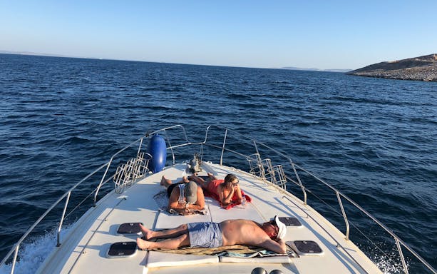 People relaxing on a yacht deck during a daily cruise to Delos and Rhenia islands.