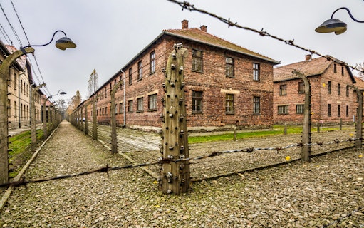 Barbed wire fence and brick buildings at Auschwitz-Birkenau concentration camp.
