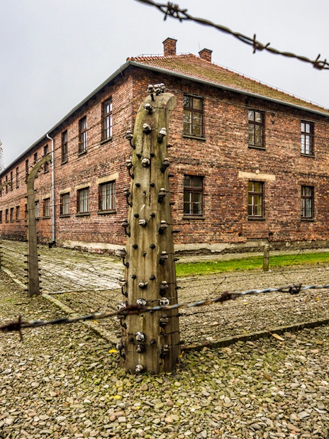 Barbed wire fence and brick buildings at Auschwitz-Birkenau concentration camp.