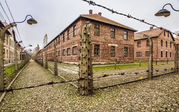 Barbed wire fence and brick buildings at Auschwitz-Birkenau concentration camp.