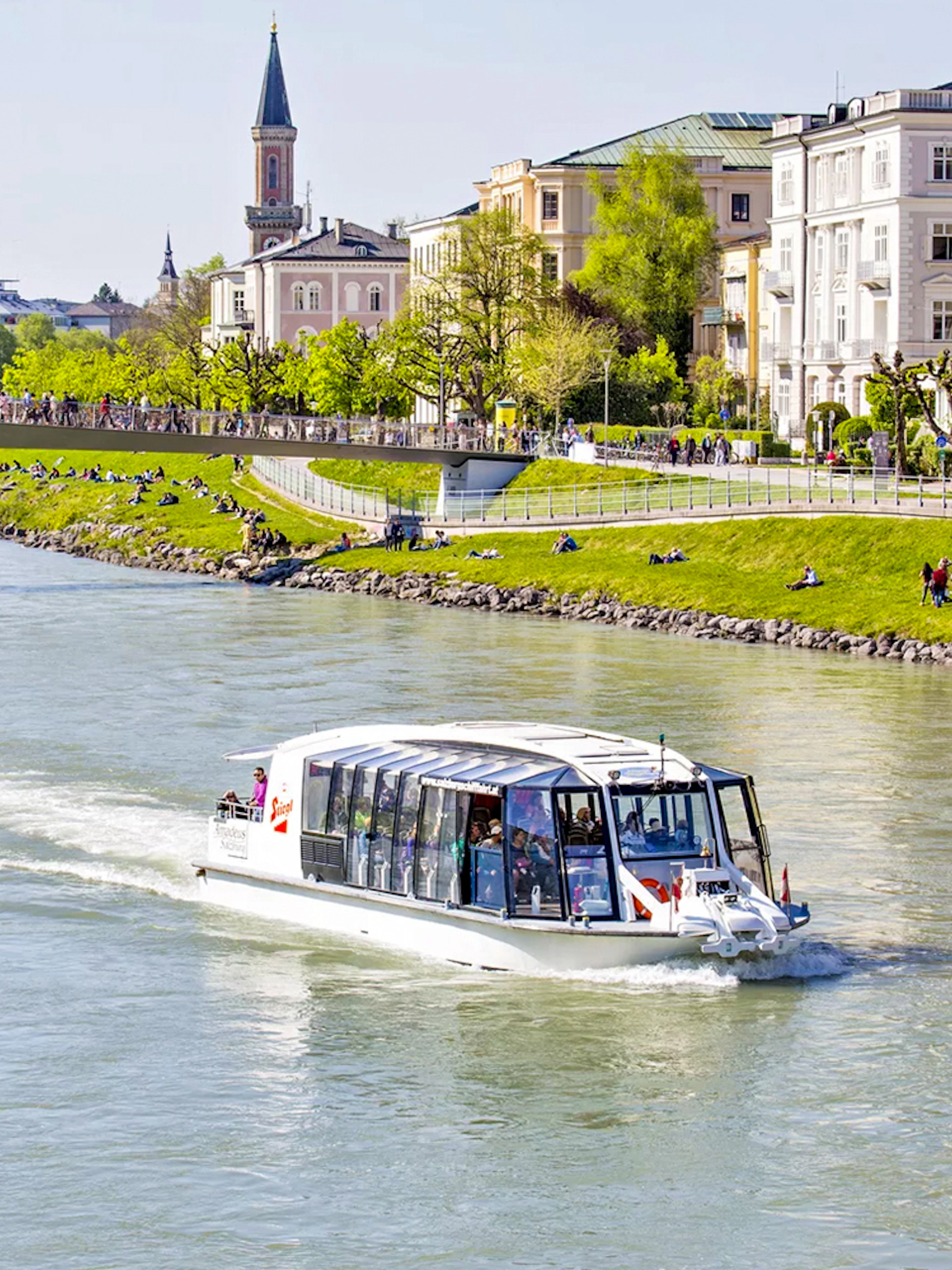 Salzburg river cruise boat on the Salzach River with cityscape and bridge in the background.