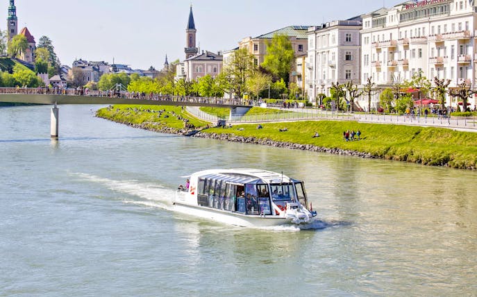Salzburg river cruise boat on the Salzach River with cityscape and bridge in the background.