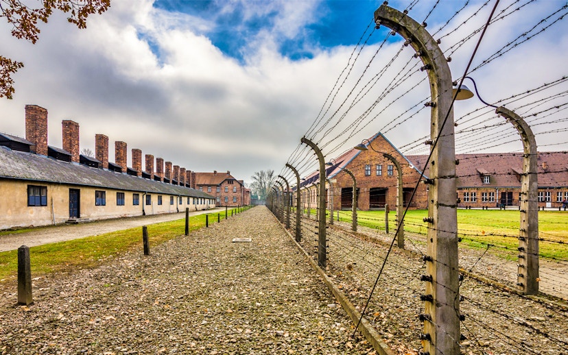 Auschwitz-Birkenau concentration camp buildings and barbed wire fence under cloudy sky.