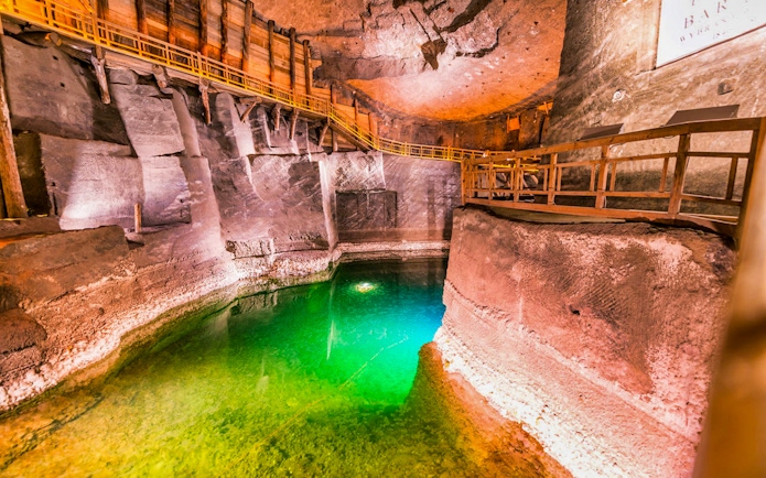 Wieliczka Salt Mine chamber with wooden walkways and illuminated green water.