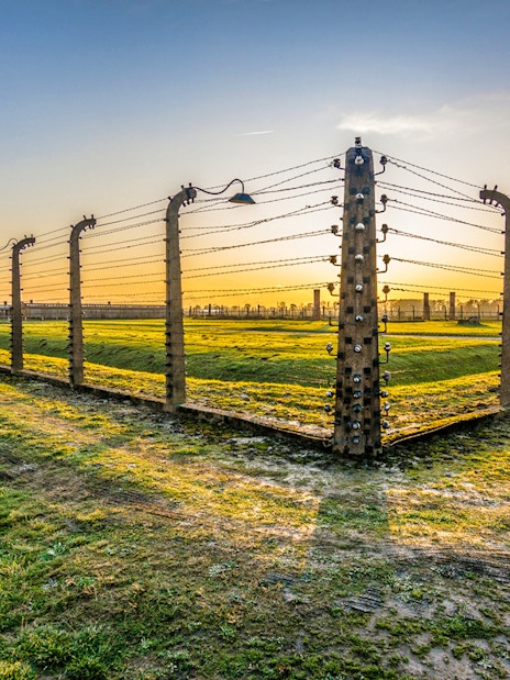 Barbed wire fence and guard tower at Auschwitz-Birkenau during sunset.