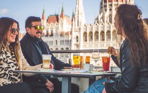 People enjoying drinks on a Budapest brunch cruise with Parliament view.