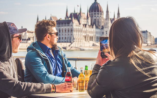 Tourists enjoying a brunch cruise on the Danube River with a view of the Hungarian Parliament in Budapest.
