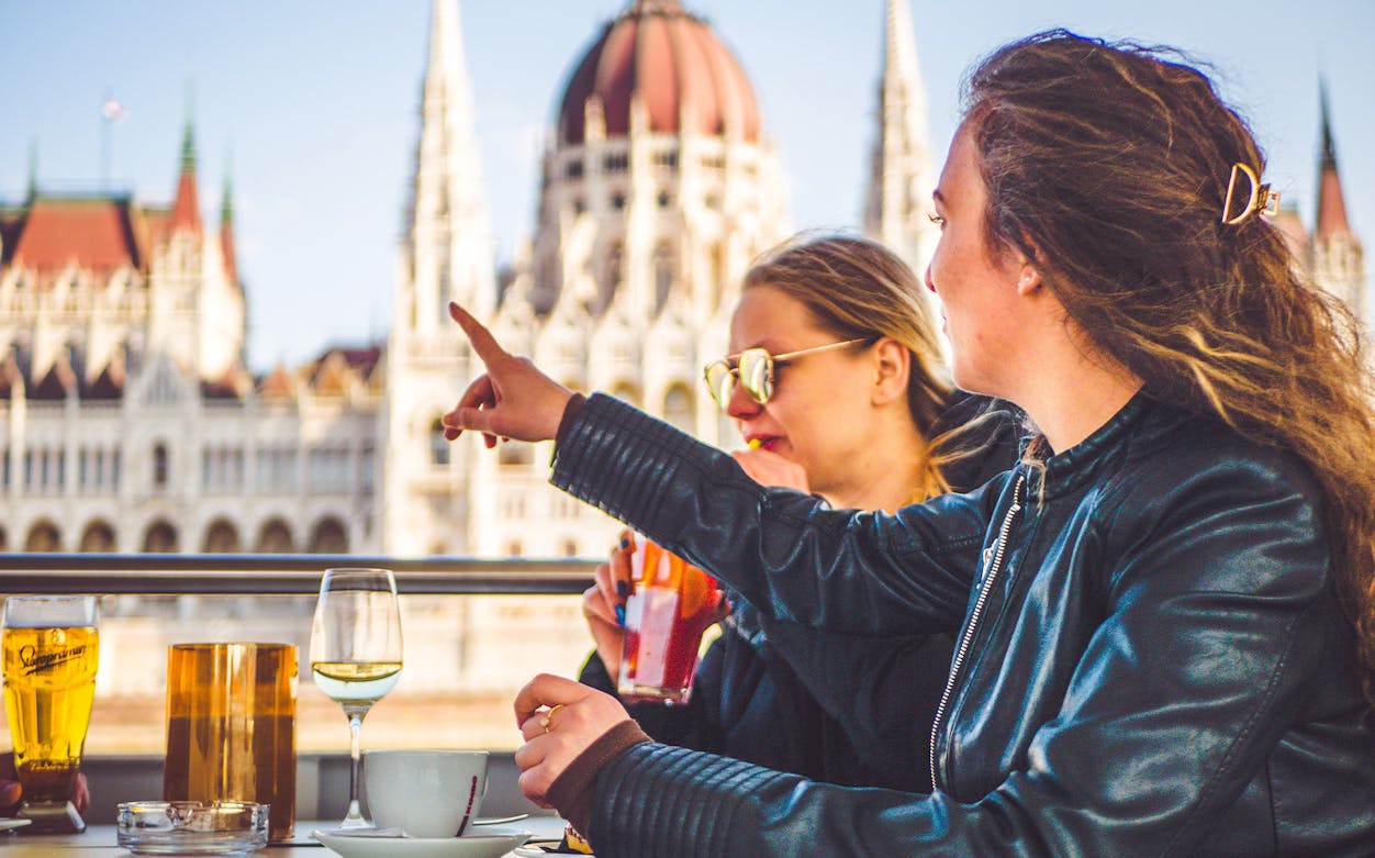 Two people enjoying drinks on a sightseeing cruise with a view of the Hungarian Parliament Building.