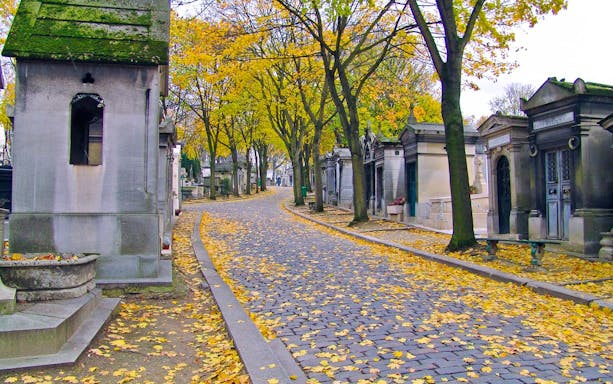 Cobblestone path lined with tombs and autumn trees at Père Lachaise Cemetery, Paris.