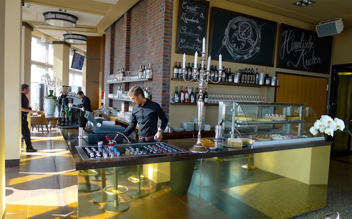 Cafe interior at Panoramapunkt Berlin with staff preparing drinks and desserts on display.