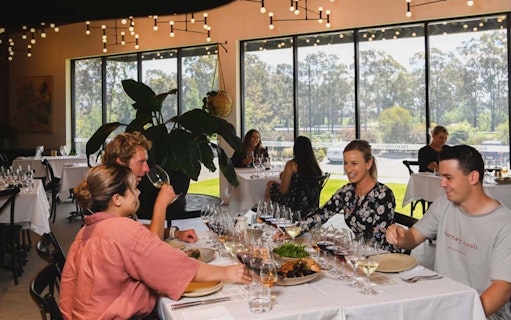 Guests enjoying wine tasting at Brokenwood winery, seated at a table with glasses and plates.