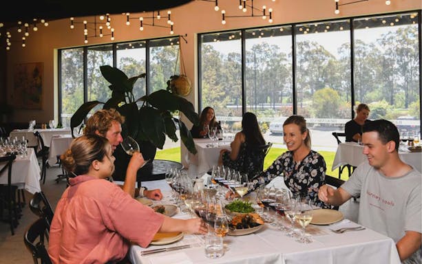 Guests enjoying wine tasting at Brokenwood winery, seated at a table with glasses and plates.