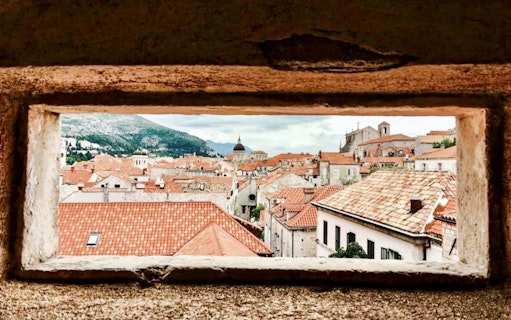 View of Dubrovnik's Old Town rooftops through a stone window, featuring historic architecture.