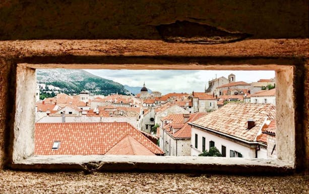 View of Dubrovnik's Old Town rooftops through a stone window, featuring historic architecture.