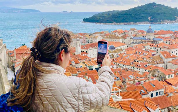 Person taking a photo of Dubrovnik's red rooftops and sea from city walls.