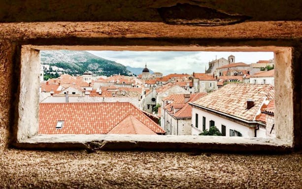 View of Dubrovnik's red-tiled rooftops through a stone window on the city walls.