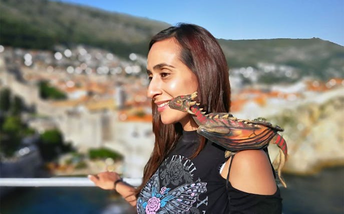 Woman with dragon figurine on shoulder, overlooking Dubrovnik's historic cityscape.