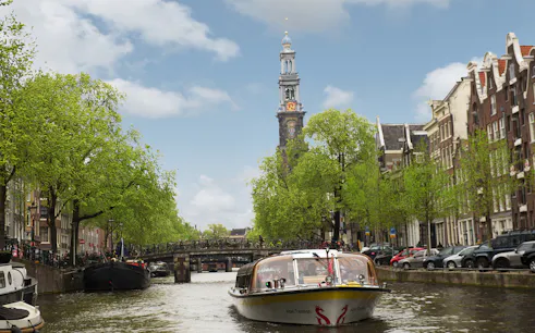 Canal boat on Amsterdam's canal with Westerkerk tower in the background.