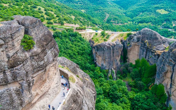 Tourists walking along a path on the cliffs of Meteora, Greece.