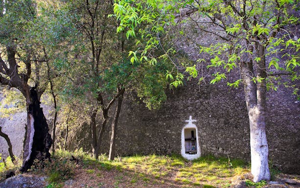Rocky landscape with a small shrine in Meteora, Greece, surrounded by trees.