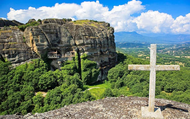 Monastery built into rock formations with a cross in Meteora, Greece.