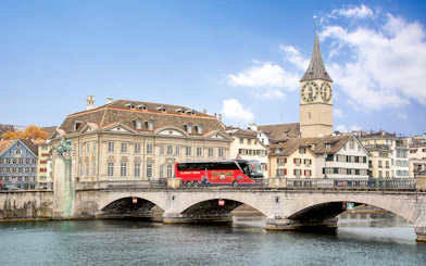 Tour bus crossing Münsterbrücke with St. Peter's Church in Zurich.
