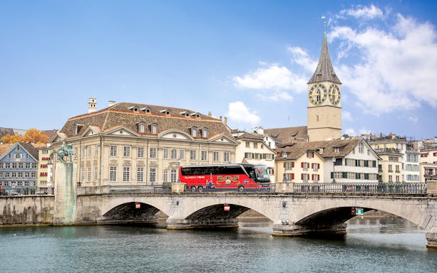 Tour bus crossing Münsterbrücke with St. Peter's Church in Zurich.